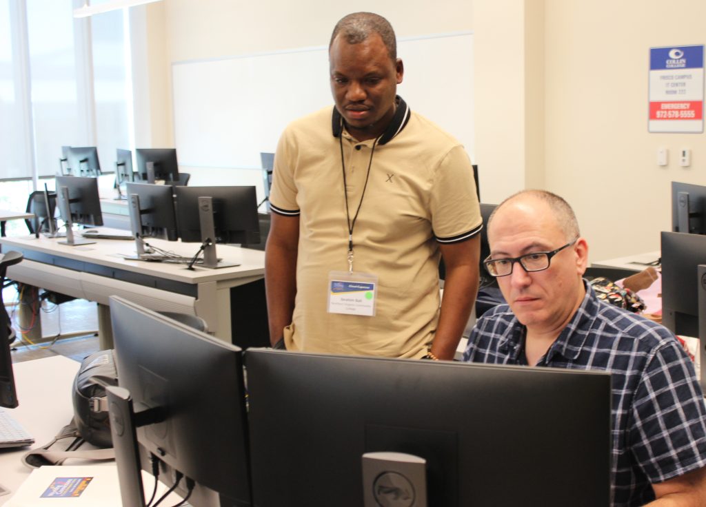 A Working Connections attendee looks over the shoulder of another attendee as they work through a virtual lab exercise in a Collin College classroom.