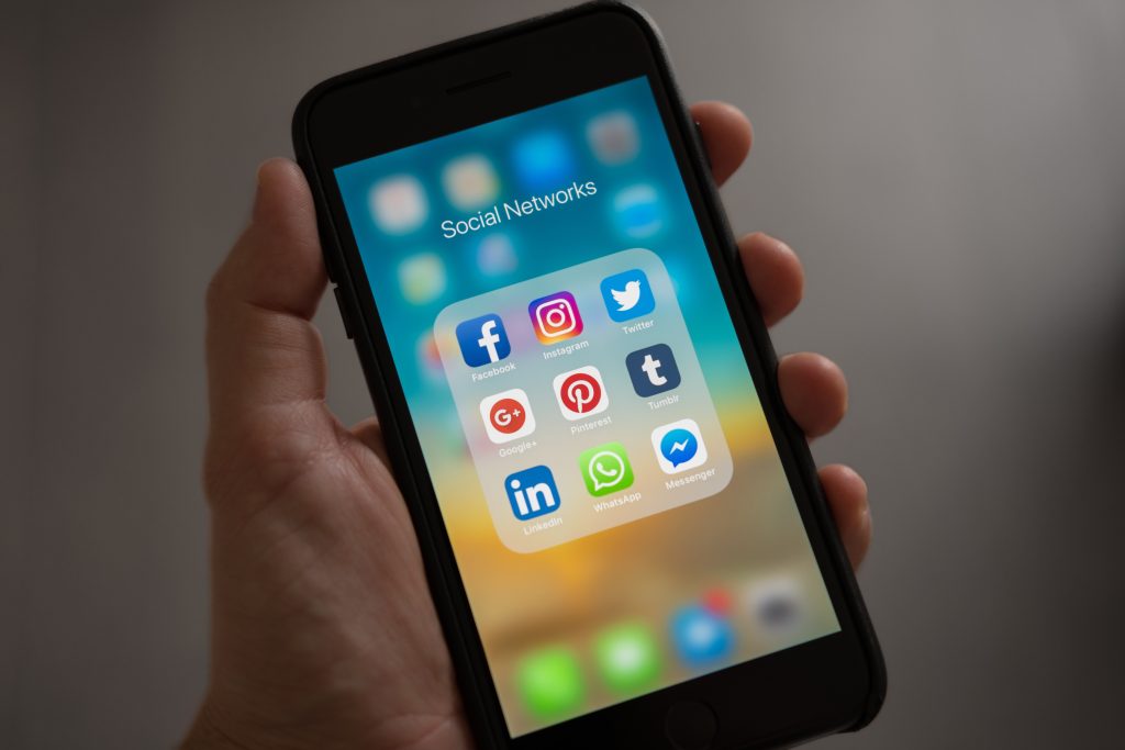 Stock photo of a hand holding a smartphone that's displaying a number of social media app icons on the home screen.