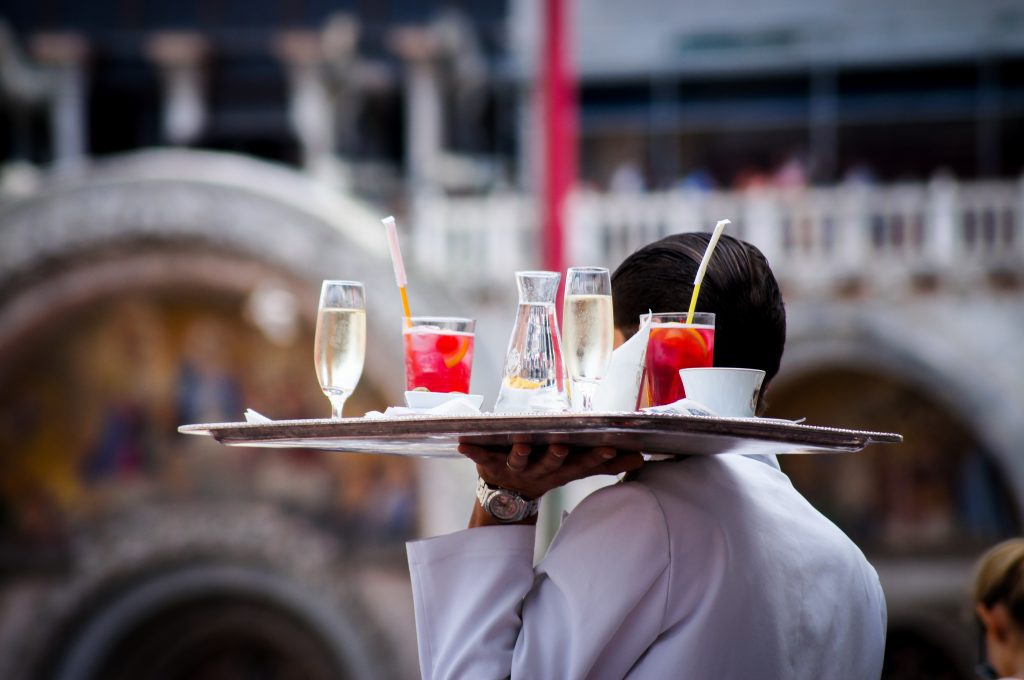 A white-coated waiter delivers a plate of drinks at an outdoor event.
