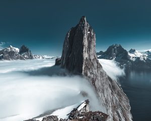 Stock photo of a stone mountain summit poking through clouds.